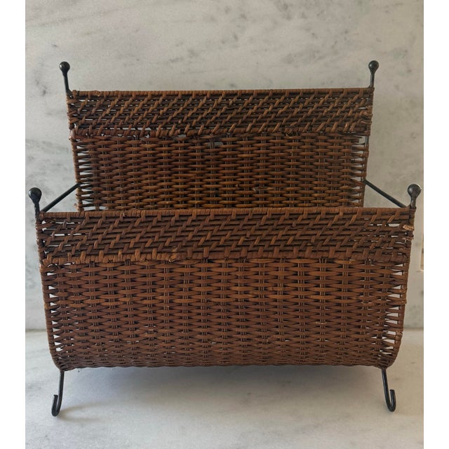 Vintage 1950s magazine rack featuring a woven wicker basket for holding magazines or newspapers and supported by a metal...