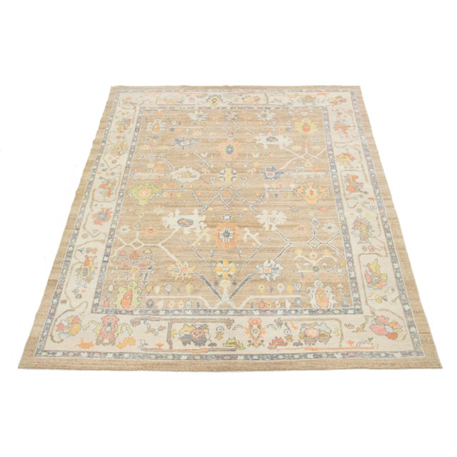 This hand-knotted wool rug is modern Turkish and features a light brown field with a captivating multicolor floral...