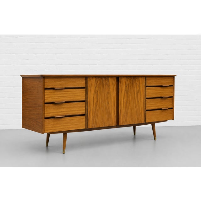Mid Century Modern Credenza crafted in olive ash wood and African teak, c. 1960’s. The cabinet features a stunning pair of...