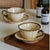 Crafted using handmade earthenware techniques, the cups and saucers feature natural beige-brown speckled textures. The...