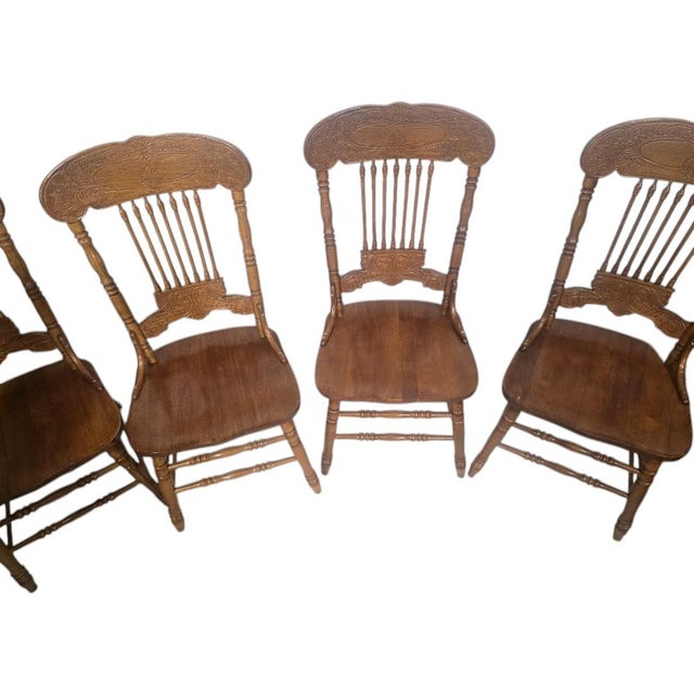 Classic set of four vintage solid oak dining chairs featuring beautifully carved pressed-back crest rails, turned spindle...