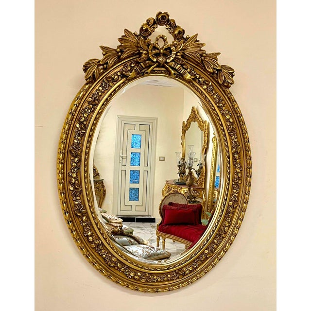 Elegant Italian style vertical oval wall mirror featuring an ornate gold leaf frame beautifully enhanced with decorative...