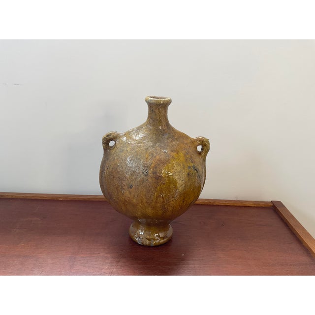 Handcrafted vintage Moroccan ceramic vessel with two applied loop handles and a rich, mustard yellow glaze showing earthy...