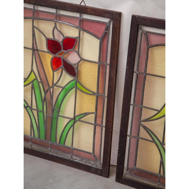 This stunning, hand-crafted stained glass panel features a vibrant red and white flower nestled among elegant green...