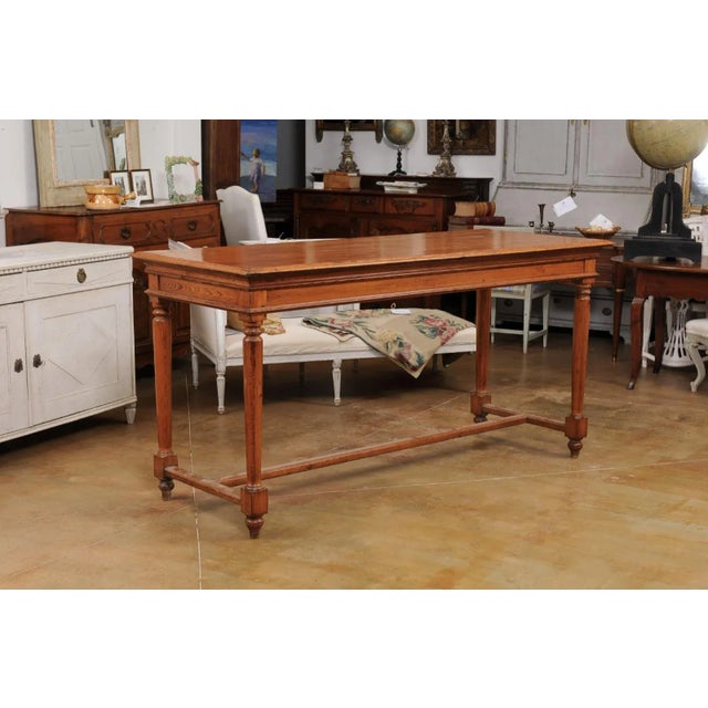 A French Louis XVI style high bar pine table from the 20th century, with cylindrical tapering legs, toupie feet and H-Form...