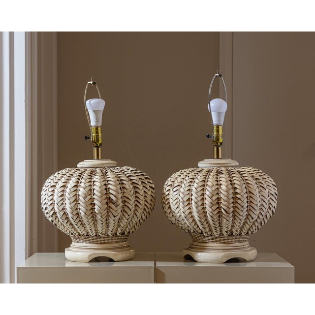 Striking matched pair of vintage table lamps featuring sculptural woven rattan bodies in an aged ivory finish. The...