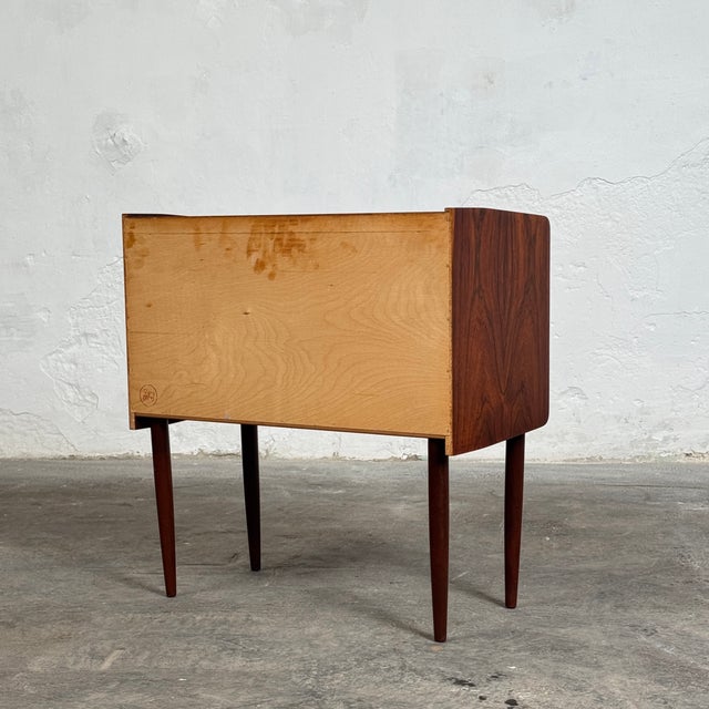 Compact mid-century Danish dresser crafted in rosewood, featuring a beautiful natural wood grain pattern that highlights...