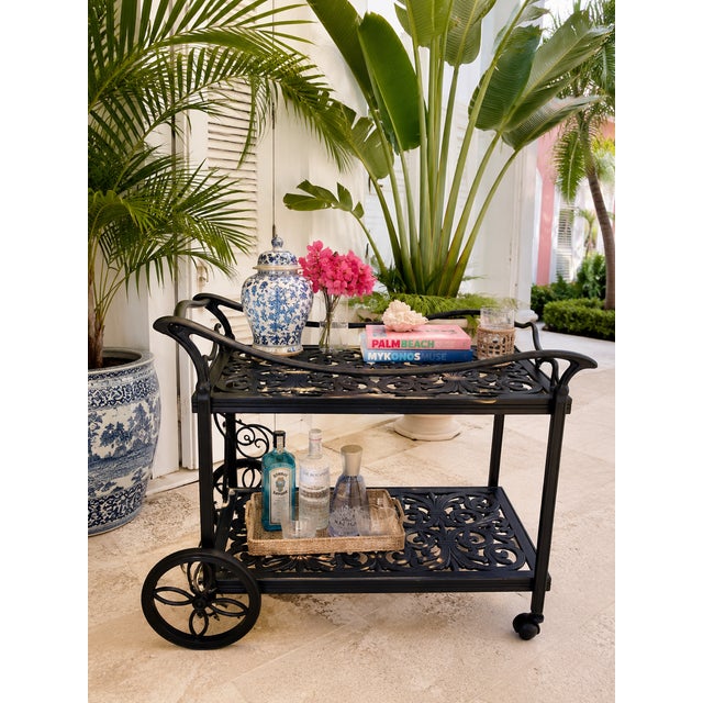 Elegant black metal bar cart featuring intricate scrollwork details and timeless Palm Beach sophistication. Beautifully...