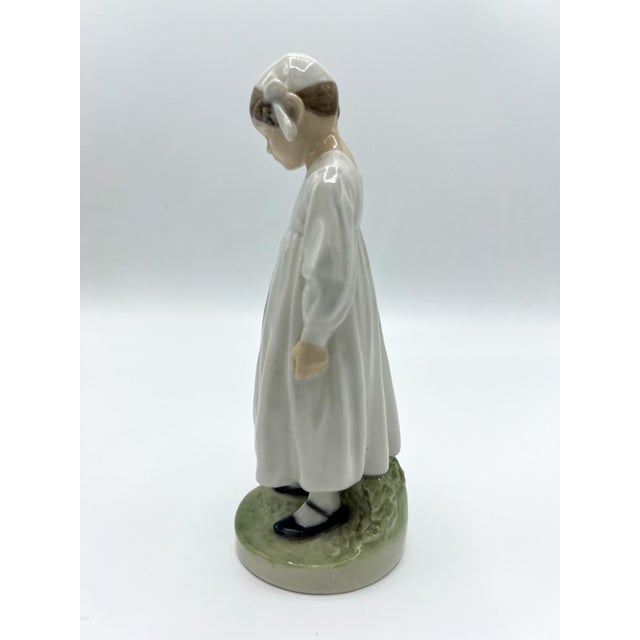 A very sweet Royal Copenhagen Porcelain Figurine Girl With Book in a white gown and cap