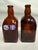 This vintage set includes two amber glass bottles featuring colorful hand-painted German designs on the front and sides....