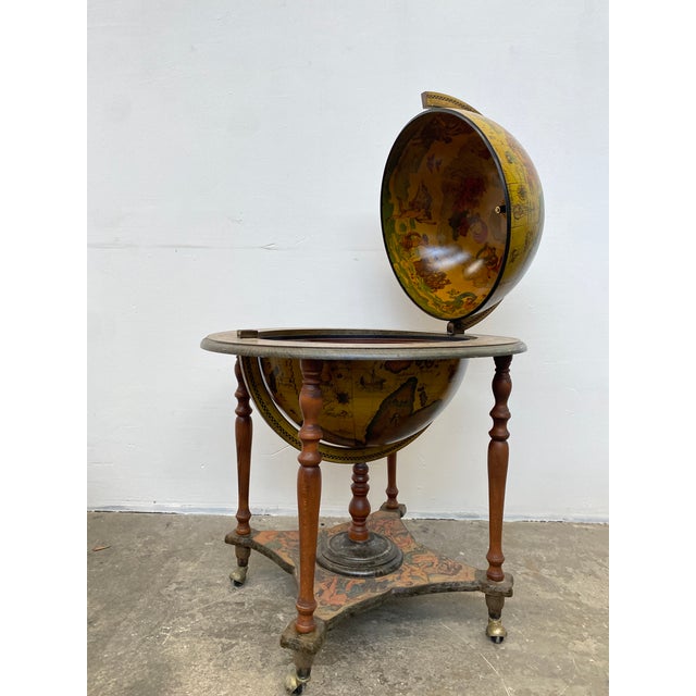 A globe bar serving table, resting on a turned wooden base with four legs joined by a stretcher and finished with brass...