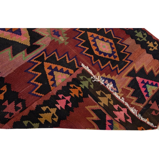 Beautiful vintage Turkish Kilim hand-knotted wool runner with a red field. This rug has a black frame and multicolor...