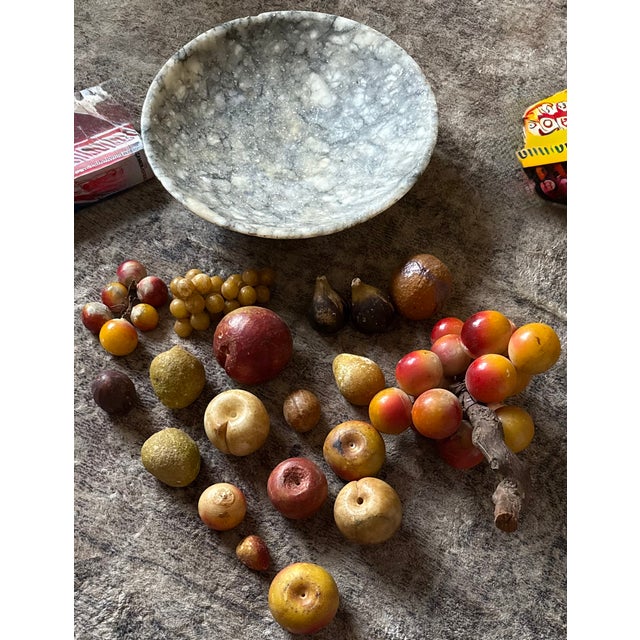 A beautifully crafted collection of hand-carved alabaster fruit rests in a shallow stone bowl, capturing the timeless...