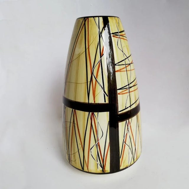 This vase is made of brown, red and yellow ceramic. It has a conical shape with black abstract decoration and hazelnut and...
