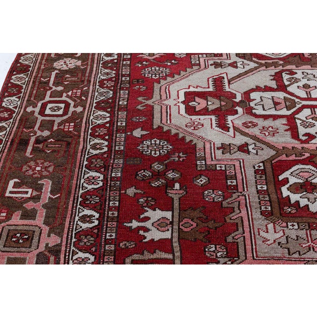 An early 20th century Persian Heriz antique rug has a burgundy background with taupe, grey, white, sage and rose accents....