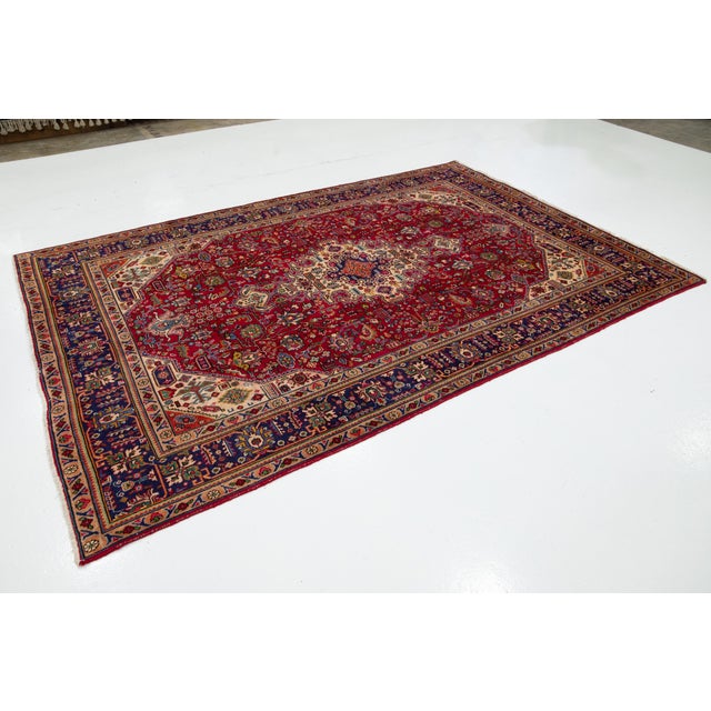 This Persian Tabriz Hand-knotted wool rug has a red field with multicolor accents featuring an allover floral design. This...