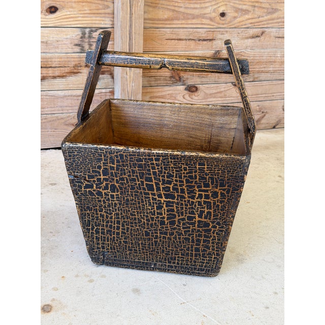 A wonderfully primitive antique wooden rice or grain bucket featuring a dramatic black crackle-painted exterior and...