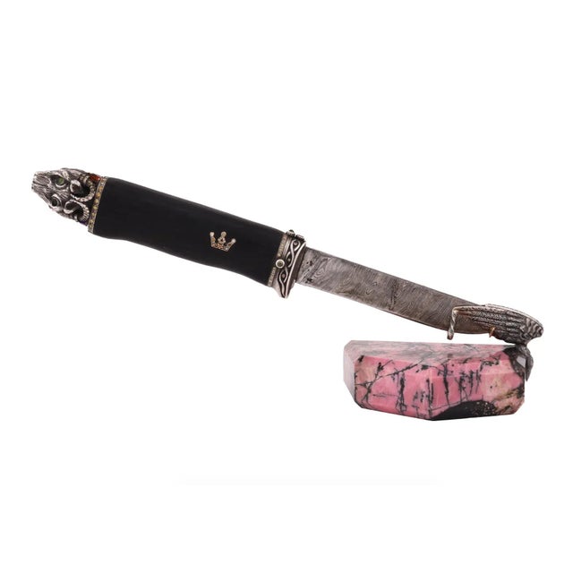 A letter opener knife with a patterned metal blade and a black wood and silver handle with two crowns. The end of the...