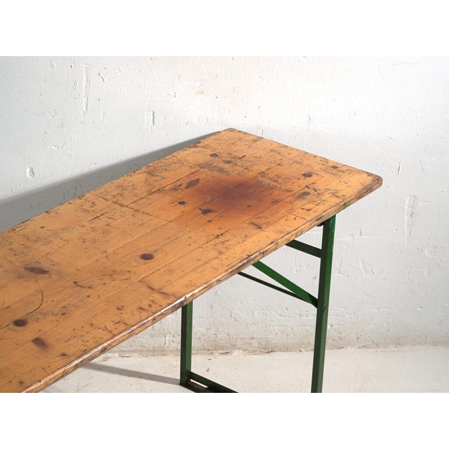 This antique beer garden table (bierzelt) in pine wood features a long solid pine top over x-shaped folding legs in green-...