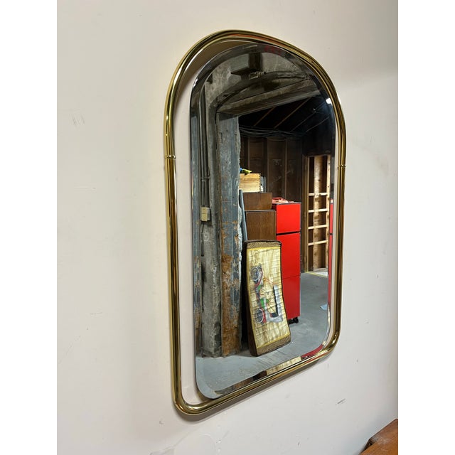 A refined example of mid-century modern design, this arched wall mirror features a sleek, sculptural brass frame with...