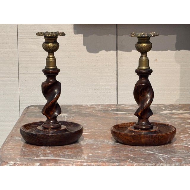 A pair of oak barley twist candlesticks with brass sconces and turned dished bases.