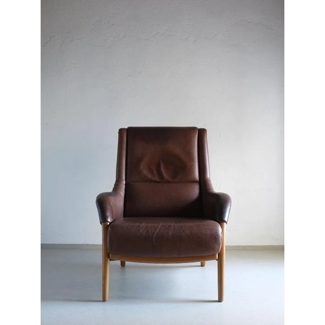 Vintage brown leather lounge chair with curved details. Dimensions: H 100 cm, H(seat) 42 cm, W(back/seat) 80/60 cm,...