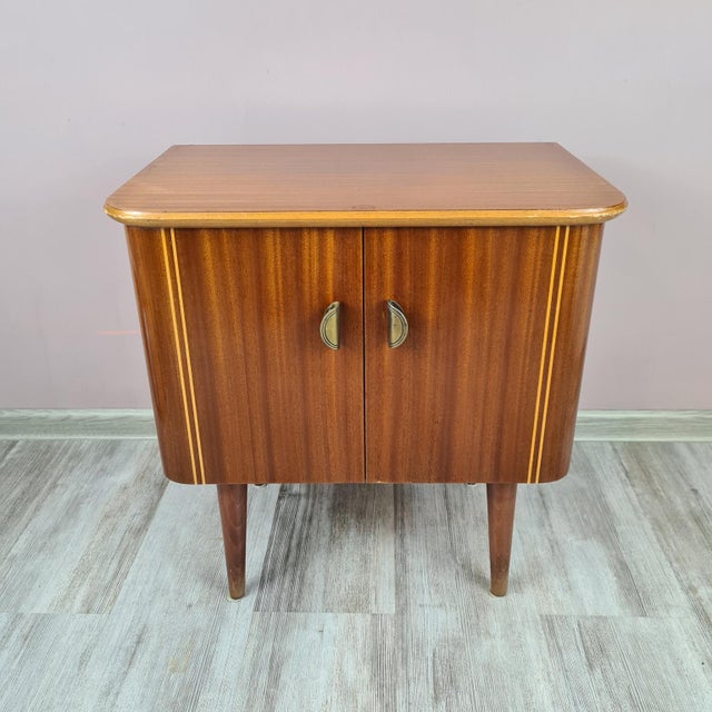 An elegant small cabinet from the Mid-Century Modern period, dating back to the 1960s. The piece is made of veneered wood...