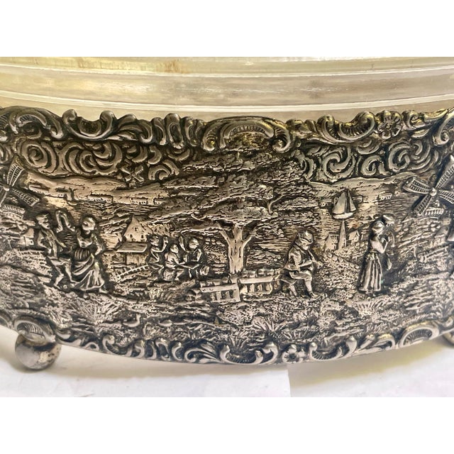 This is a very sweet silver plate casserole holder with four ball feet and a traditional Dutch embossed scene of people...