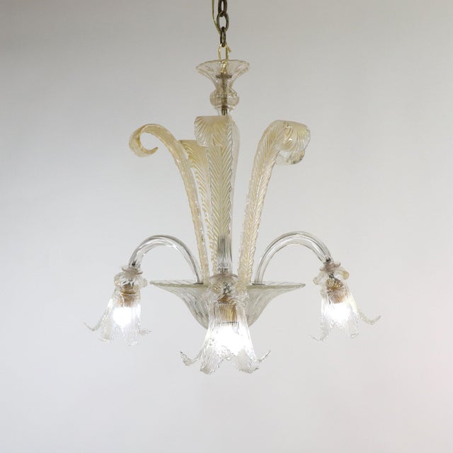 This beautifully handcrafted mid-century gold-infused Cristallo Murano chandelier features three scroll arms with lily-...