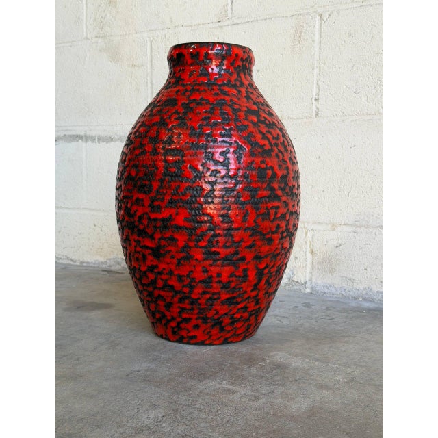 This striking ceramic floor vase features a vibrant red and black lava glaze with a bulbous silhouette. The bold texture...