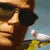 This oil on panel artwork features a figure wearing sunglasses, adorned with small model airplanes and surrounded by...