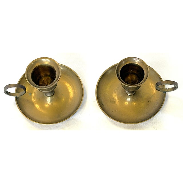 Vintage pair of solid brass chamberstick candle holders from the mid 20th century. Each has a finger handle, and one...