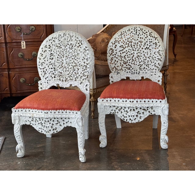 Pair of painted white carved side chairs with densely pierced floral work across the backs, aprons, and legs. The carving...