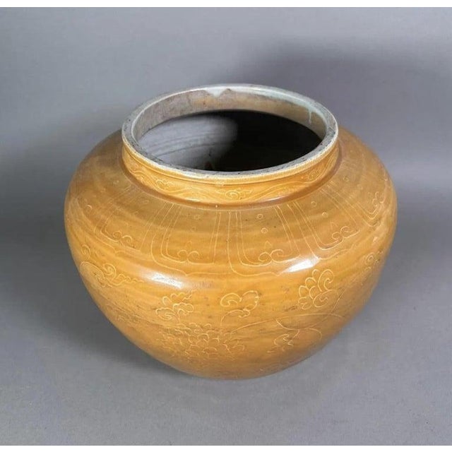 A rounded ceramic vessel finished in a warm mustard glaze, decorated throughout with finely incised floral and scrolling...