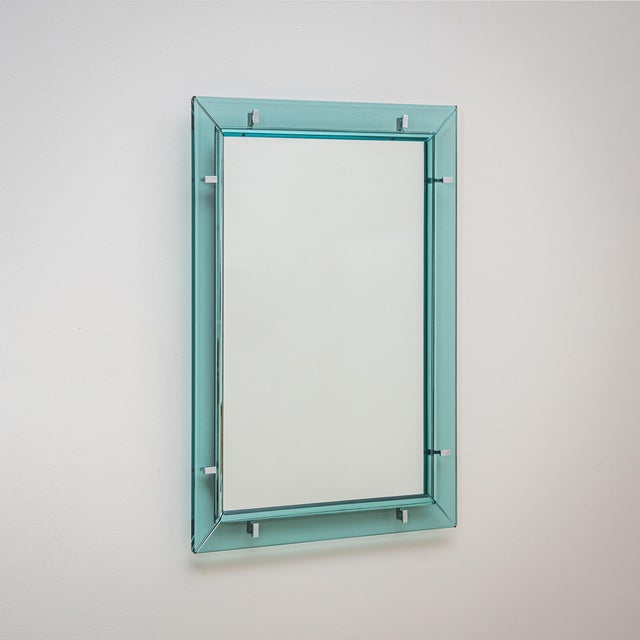 Rectangular wall mirror with a light blue transparent glass frame featuring a faceted inner edge. The piece exemplifies...