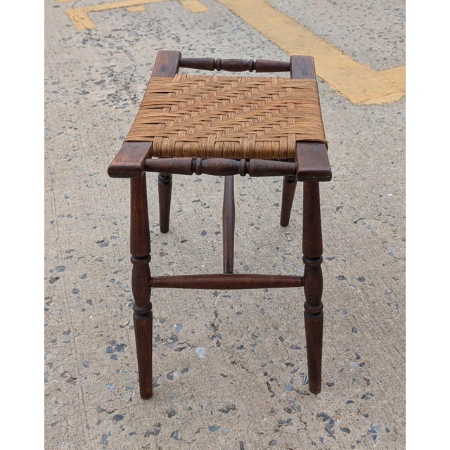 Embodying timeless American craftsmanship, this vintage early-to-mid-20th-century stool features a hand-woven wicker seat...