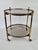 An elegant vintage serving/bar table on wheels, made of brass and featuring two panels of mirrored glass. The piece is...