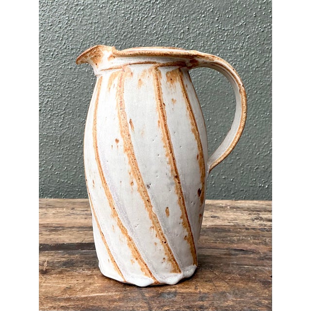 This sculptural studio pottery pitcher is a compelling testament to artisanal skill and organic beauty. The hand-thrown...