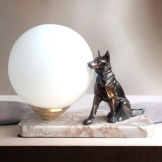 A signed vintage tedd table lamp pairing a seated german shepherd with a luminous white opaline glass globe on a veined...