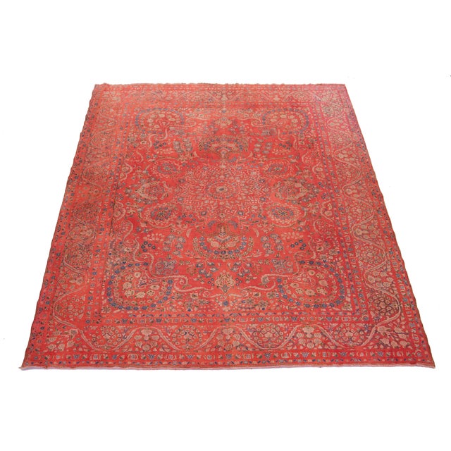 This antique red Overdyed Persian wool rug features a rosette design with blue, beige, and green accents. This rug...