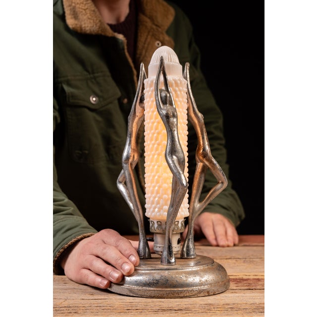 Art Deco figural table lamp featuring three stylized female figures arranged symmetrically around a central illuminated...