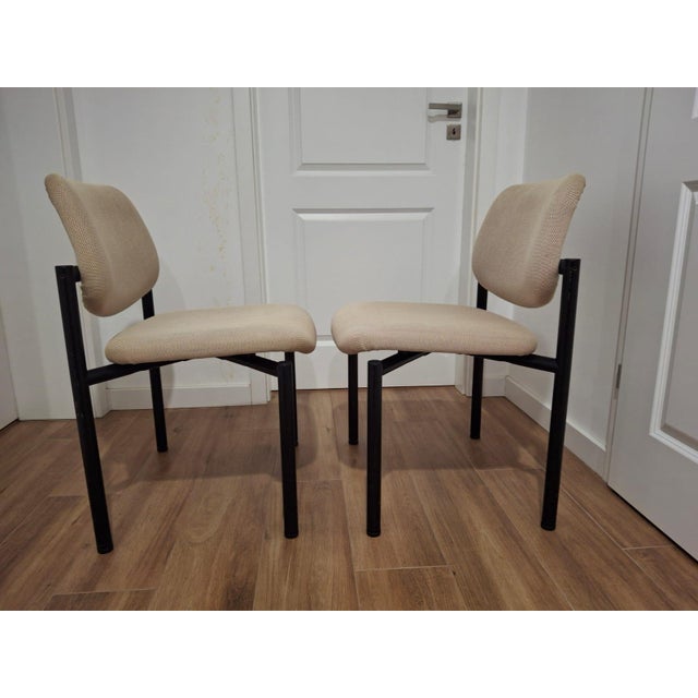 The structure features a black metal frame, with an upholstered seat and backrest in a light beige textured fabric. The...