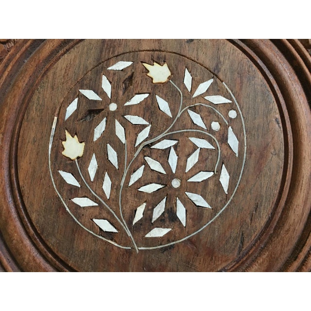 A round folding table made of teak wood, entirely carved on a support tripod.