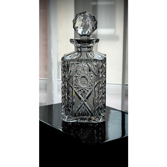 Vintage cut crystal decanter featuring a square body and detailed geometric cutting, including a central pinwheel motif...