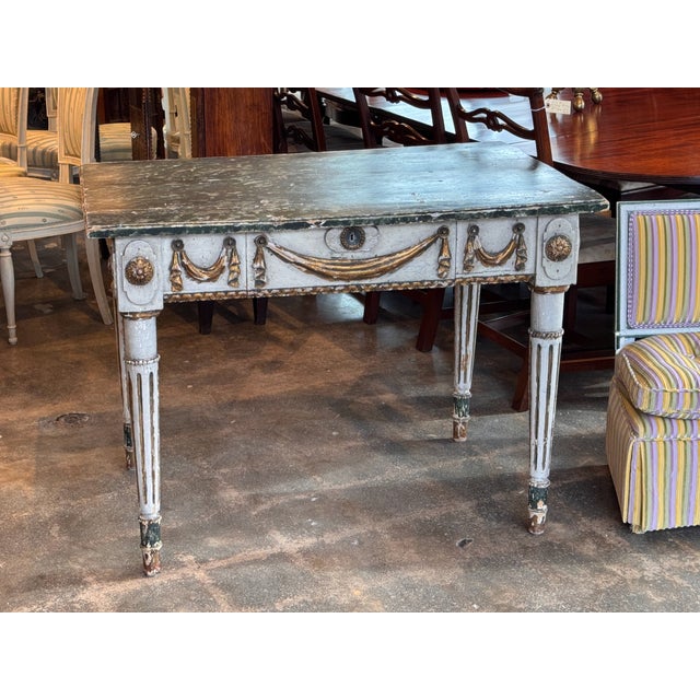 An Italian console table with a painted top above a single long drawer. The frieze is carved with a central swag and...