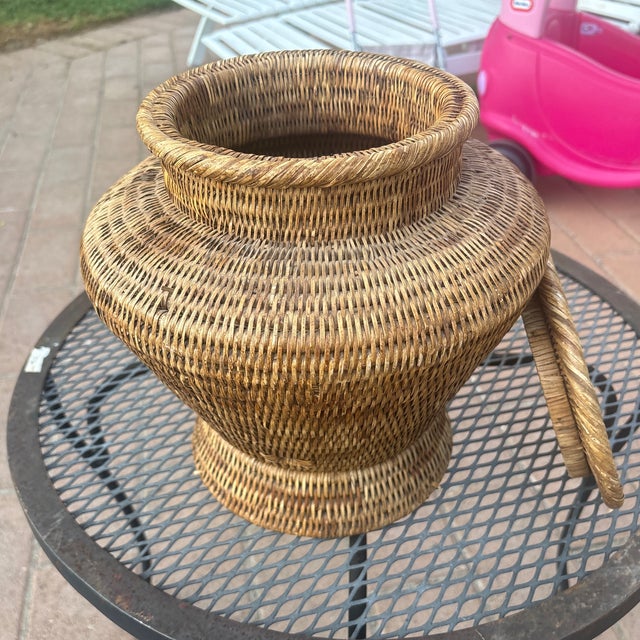 This vintage lidded woven rattan ginger jar features intricate natural cane detailing and a traditional urn silhouette....