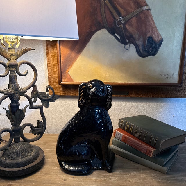 This is a 19th-century Black Jackfield Staffordshire spaniel figurine featuring a glossy black glaze and gilded gold...