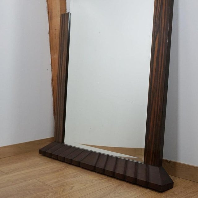 An Art Deco over mantel mirror with macassar ebony frame and a fluted, angled base. Dimensions: H 143cm W 118cm D 11cm...