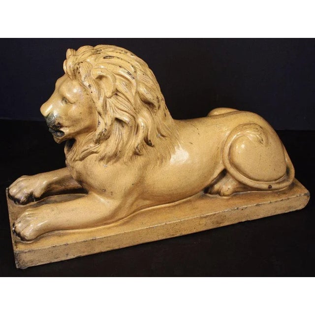 A large English lion figurine of glazed stoneware featuring a recumbent lion with fine modelling to the head and body....