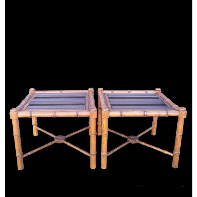 A pair of vintage large square faux bamboo side end tables. The tables feature real wood faux bamboo with smoked glass...